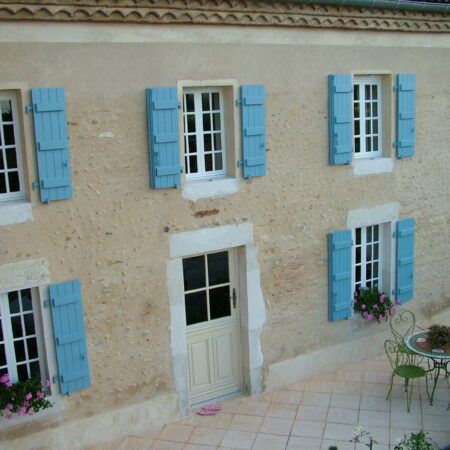 Volets bleus maison murs beiges fenêtres fleurs